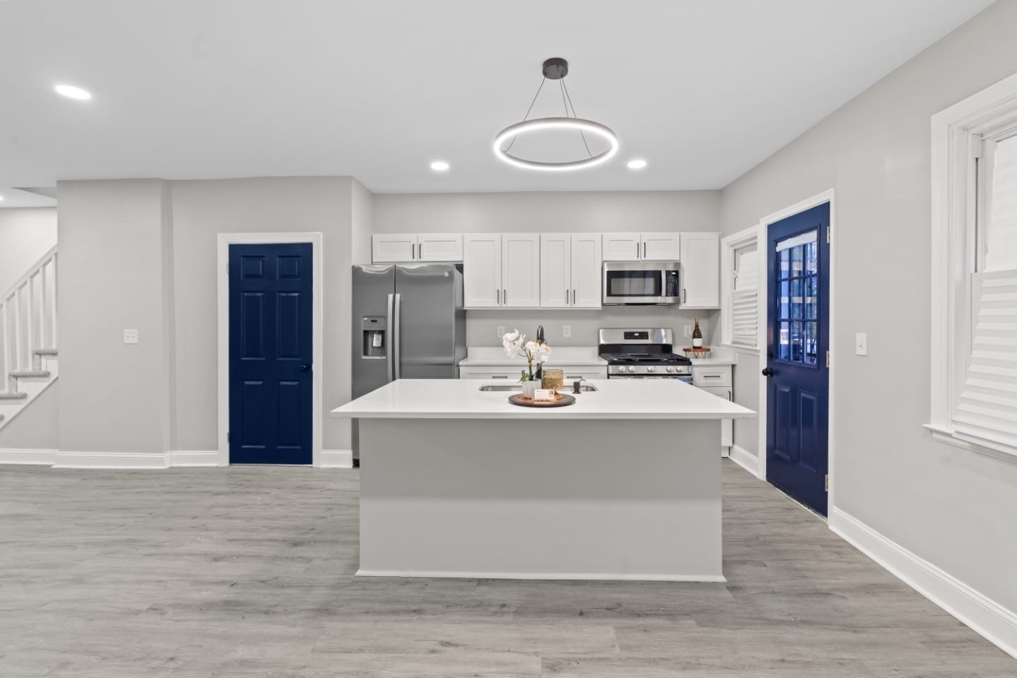 Open-concept kitchen with white cabinetry, quartz island and navy doors